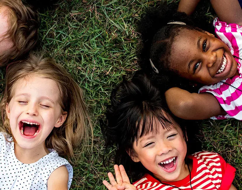 Tre bambini piccoli di diverse etnie sdraiati sull'erba, che sorridono e ridono insieme