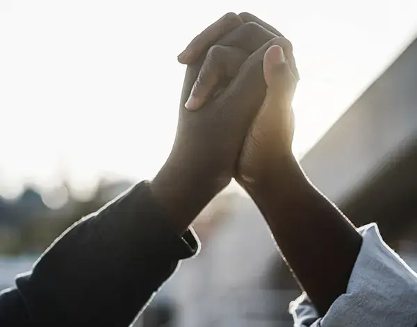 Due persone che alzano e uniscono le mani all'aperto, stagliate contro la luce brillante del sole.