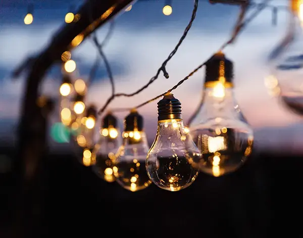 Luci decorative con lampadine luminose appese all'aperto al tramonto, che creano un'atmosfera calda.