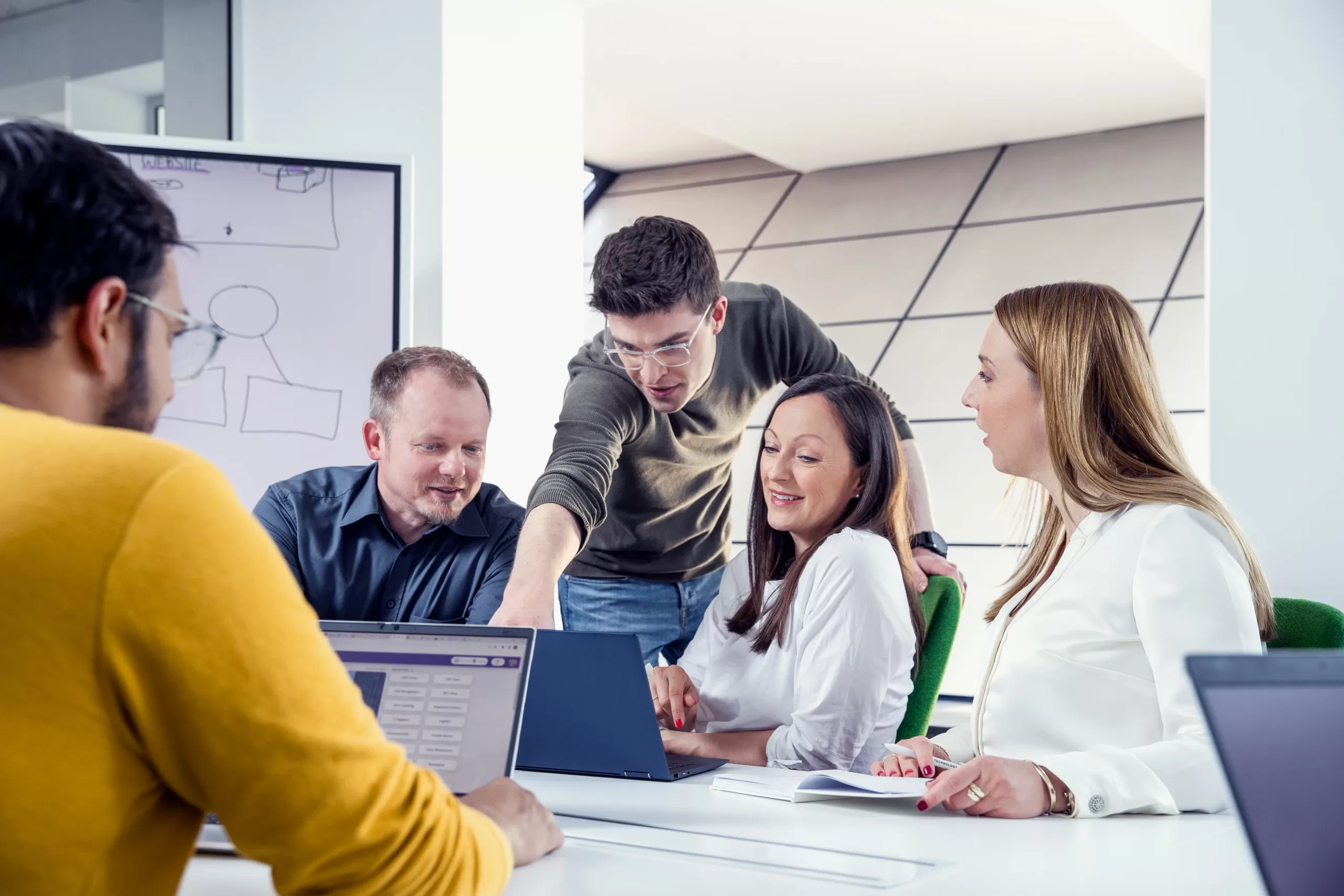 Colleagues discussing work around a laptop in a meeting room.