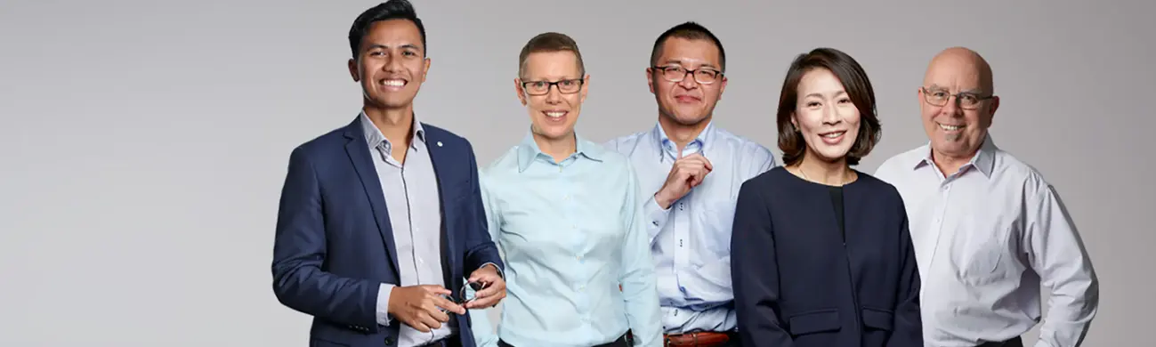 Groupe de cinq professionnels diversifiés debout ensemble devant un fond neutre, souriant avec assurance en tenue professionnelle.