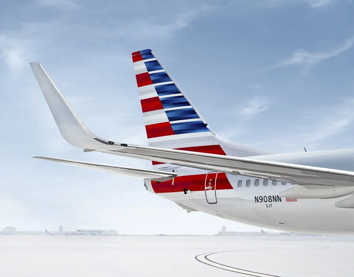Nahaufnahme eines Flugzeughecks mit roten, weißen und blauen Streifen, das auf einem verschneiten Rollfeld geparkt ist.